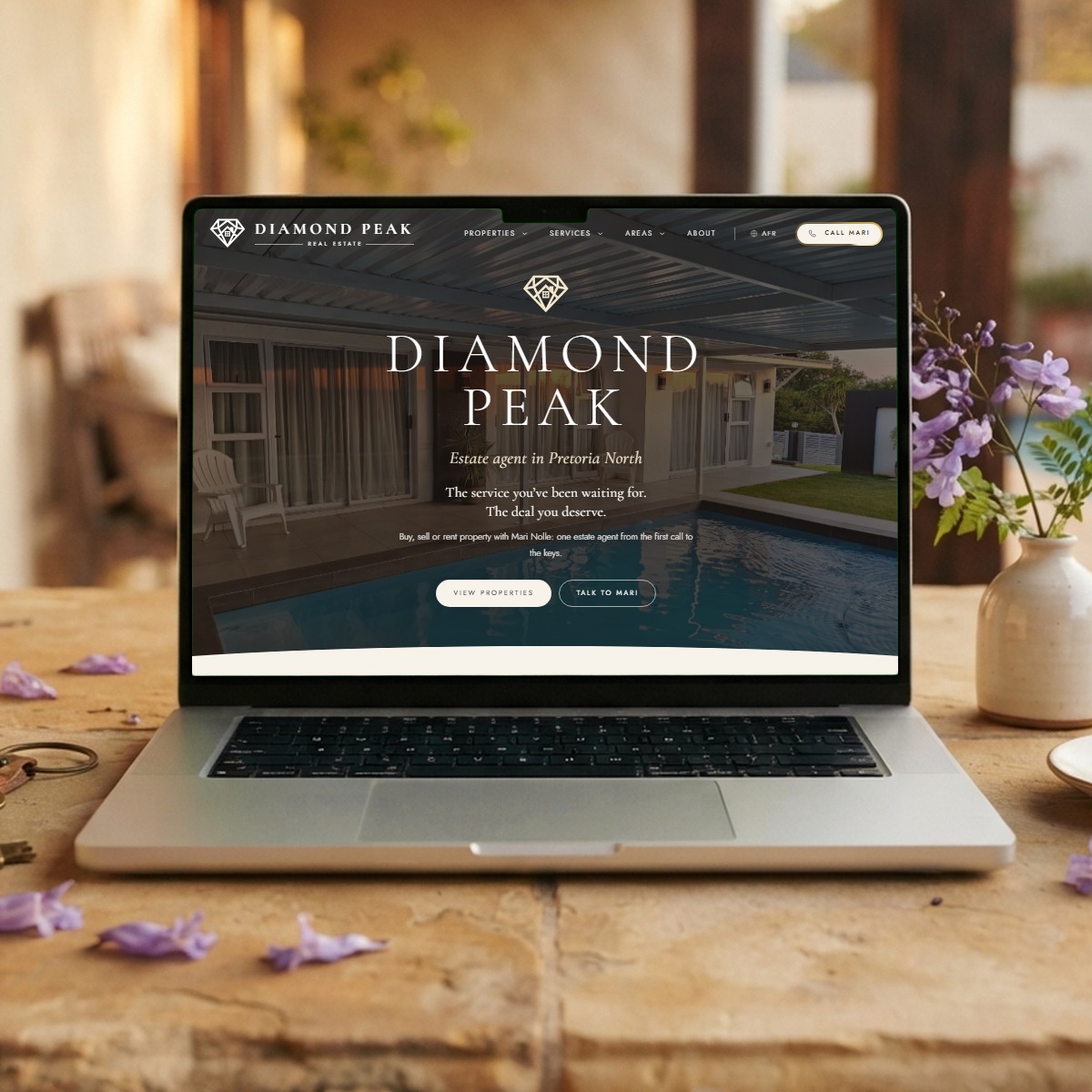 Diamond Peak estate agent website on a laptop, on a sandstone table with jacaranda blossoms